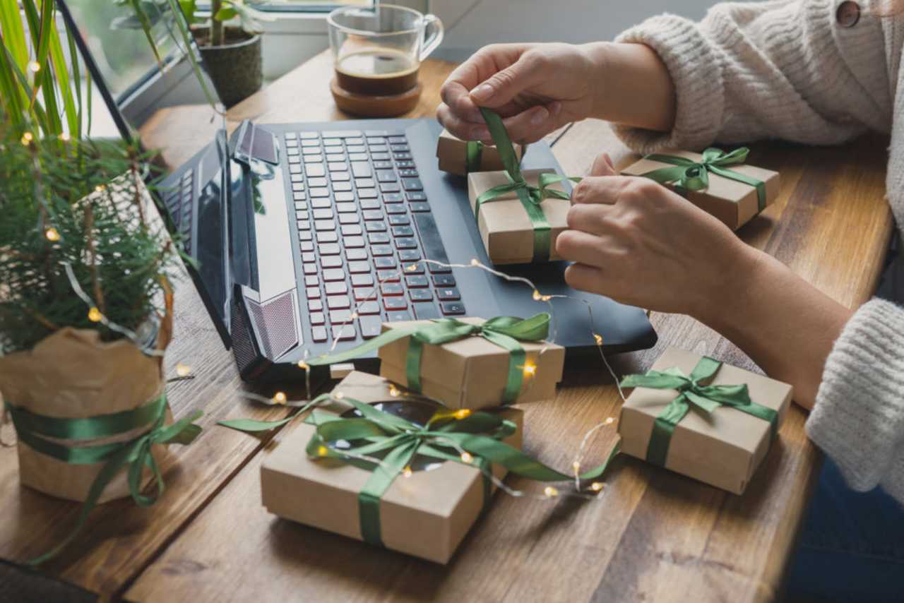woman wrapping Christmas presents at desk with laptop